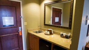 Une petite salle de bain d’hôtel comprenant un lavabo, un miroir et une porte sur laquelle est affiché un plan d’évacuation.