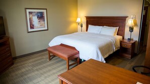Une chambre d’hôtel avec un grand lit, deux tables de chevet avec des lampes, un banc en bois, un bureau et une commode.