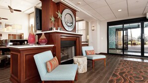 A lobby with a fireplace, two patterned armchairs, a wooden reception desk, and a patterned carpet. - Hampton Inn & Suites Navarre (Navarre)