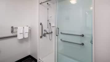 Un baño moderno con cabina de ducha de vidrio, un perchero con toallas blancas y una puerta de vidrio con manija.