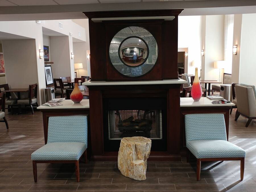 Un hall con chimenea, dos sillones estampados, un espejo redondo y una recepción.