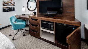 A hotel room with a wooden desk, a flat-screen TV, a microwave, a chair, and artwork on the wall. - Hampton Inn & Suites Navarre (Navarre)
