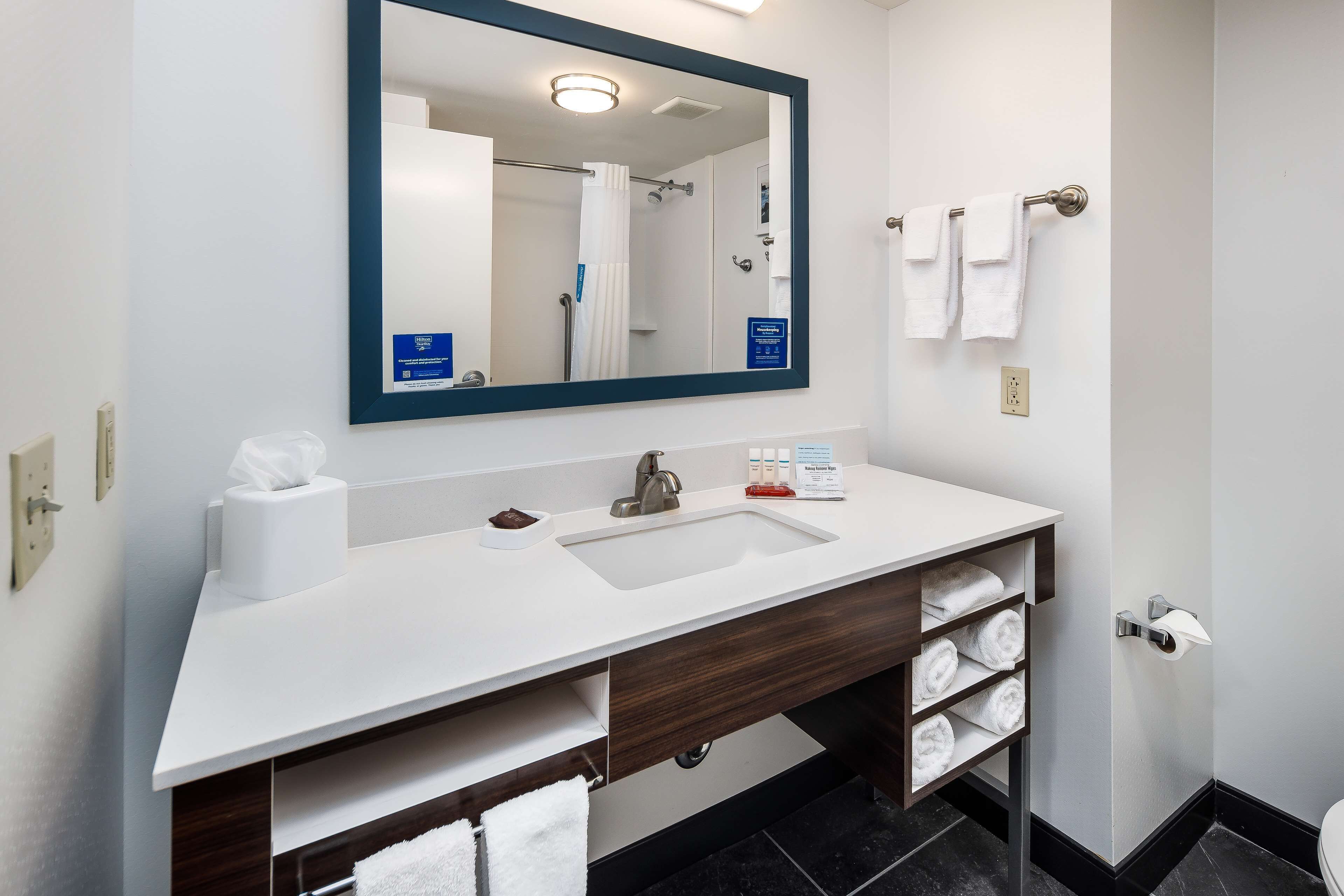 A modern bathroom with a white sink, dark wood vanity, a large mirror, and a shower visible in the reflection.