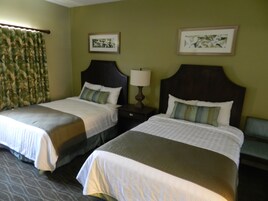 Two double beds with headboards, a nightstand with a lamp, and two framed pictures on the wall.