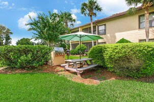 A picnic table with a green umbrella, surrounded by well-maintained hedges and a grassy lawn.