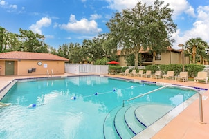A swimming pool with a tiled deck, lounge chairs, and a building with a clock.
