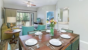 A dining area with a wooden table set for four, a vase with flowers, and a ceiling fan. - Alhambra Villas by Coolvacay (Kissimmee)