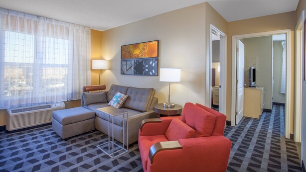 A hotel room with a sofa, ottoman, two lamps, a flat-screen TV, and a painting on the wall. - TownePlace Suites by Marriott Huntsville (Huntsville)