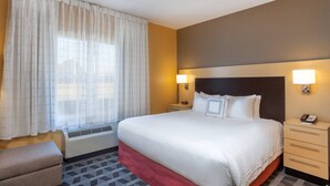 A hotel room with a large bed, bedside lamps, a heater, a small bedside table, and a telephone. - TownePlace Suites by Marriott Huntsville (Huntsville)