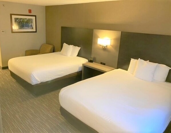 A hotel room with two beds, a nightstand, a chair, a framed picture on the wall, and a wall-mounted light.