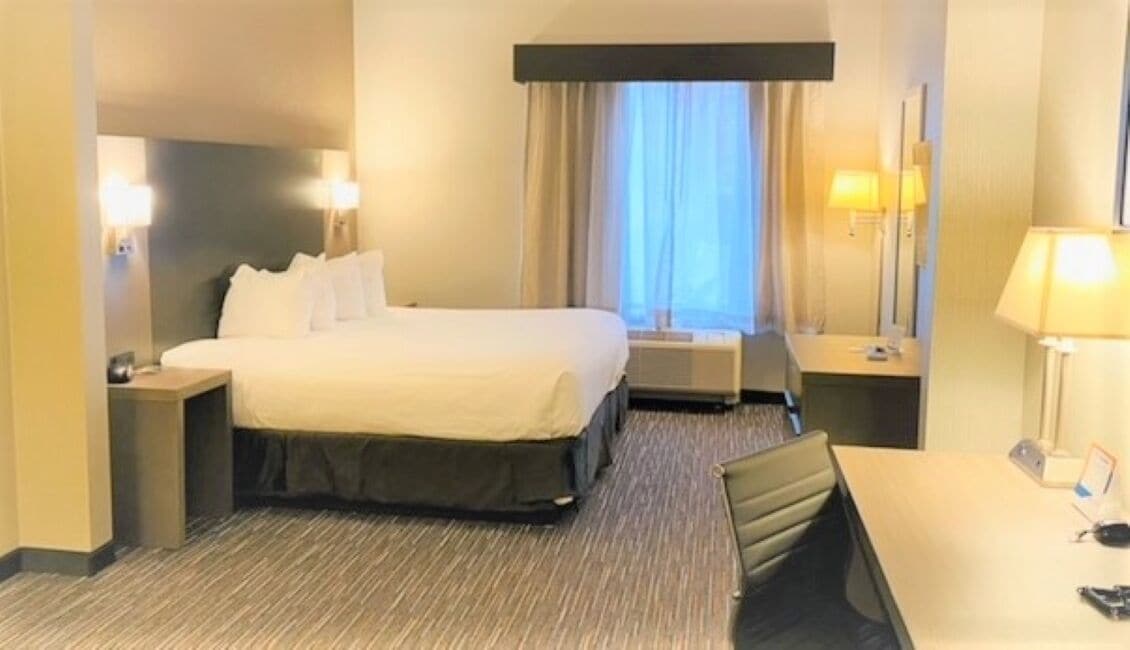 Quarto de hotel com cama, mesas de cabeceira, escrivaninha e uma cadeira.