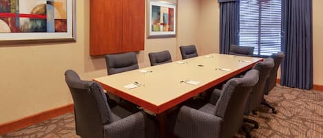 A conference room with a long table, six chairs, and two framed artworks on the walls.