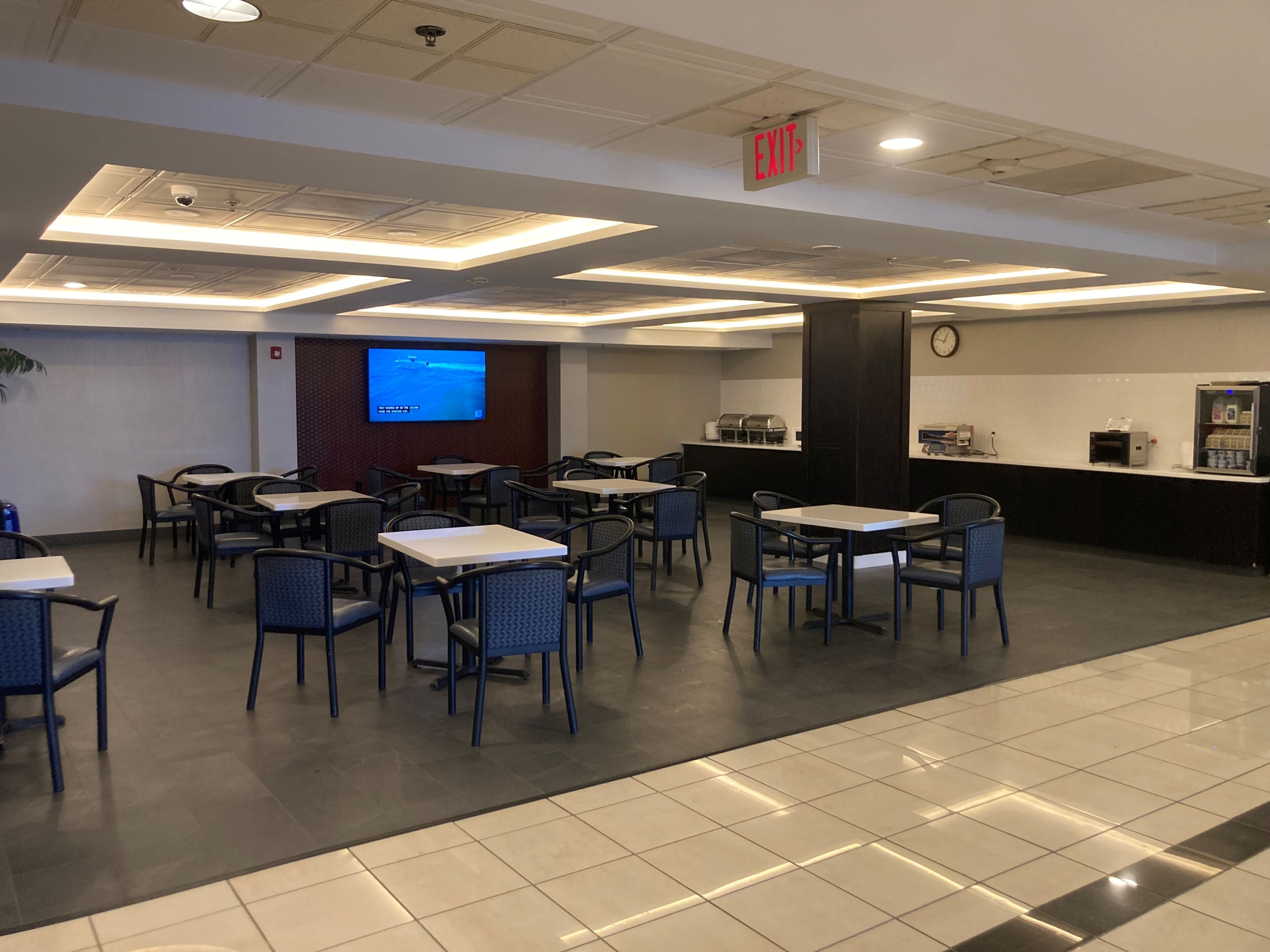 A conference room with tables and chairs, a screen, a clock, and a coffee station.