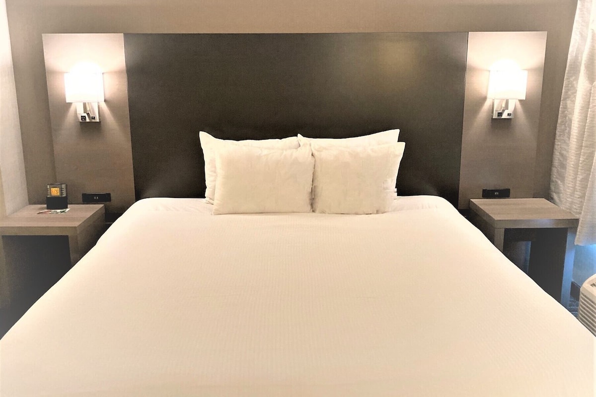 Una habitación de hotel con una cama grande, dos mesitas de noche y lámparas fijadas a la pared.