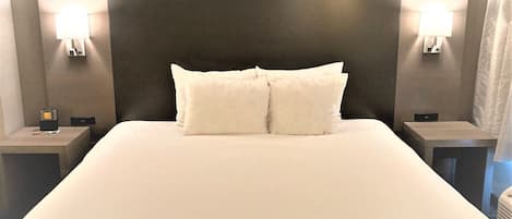 A hotel room with a large bed, two bedside tables, and wall-mounted lamps.