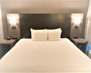 A hotel room with a large bed, two bedside tables, and wall-mounted lamps. - Wingate by Wyndham Erie (Erie)