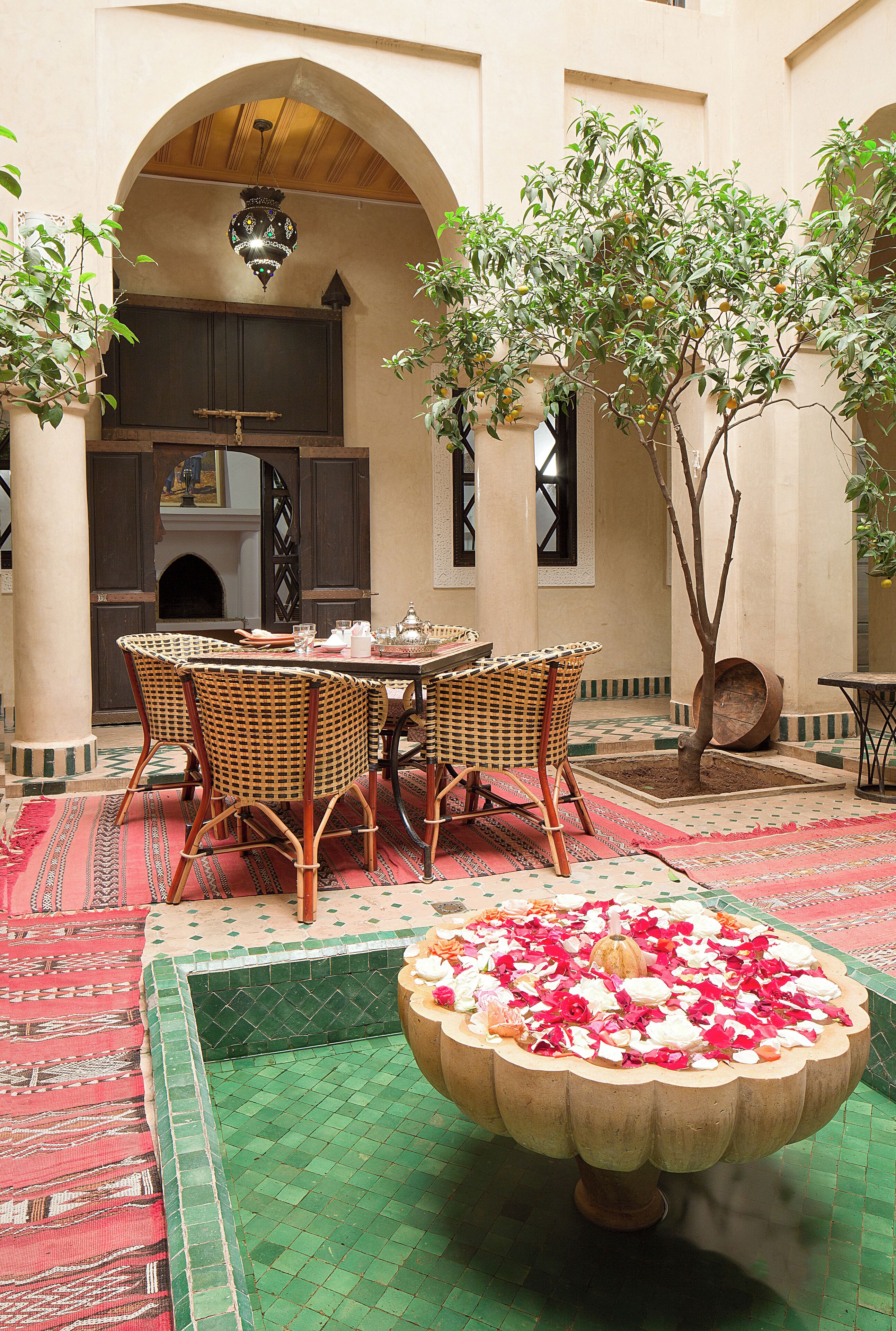 Un patio con zona de comedor, una fuente decorativa y un árbol.