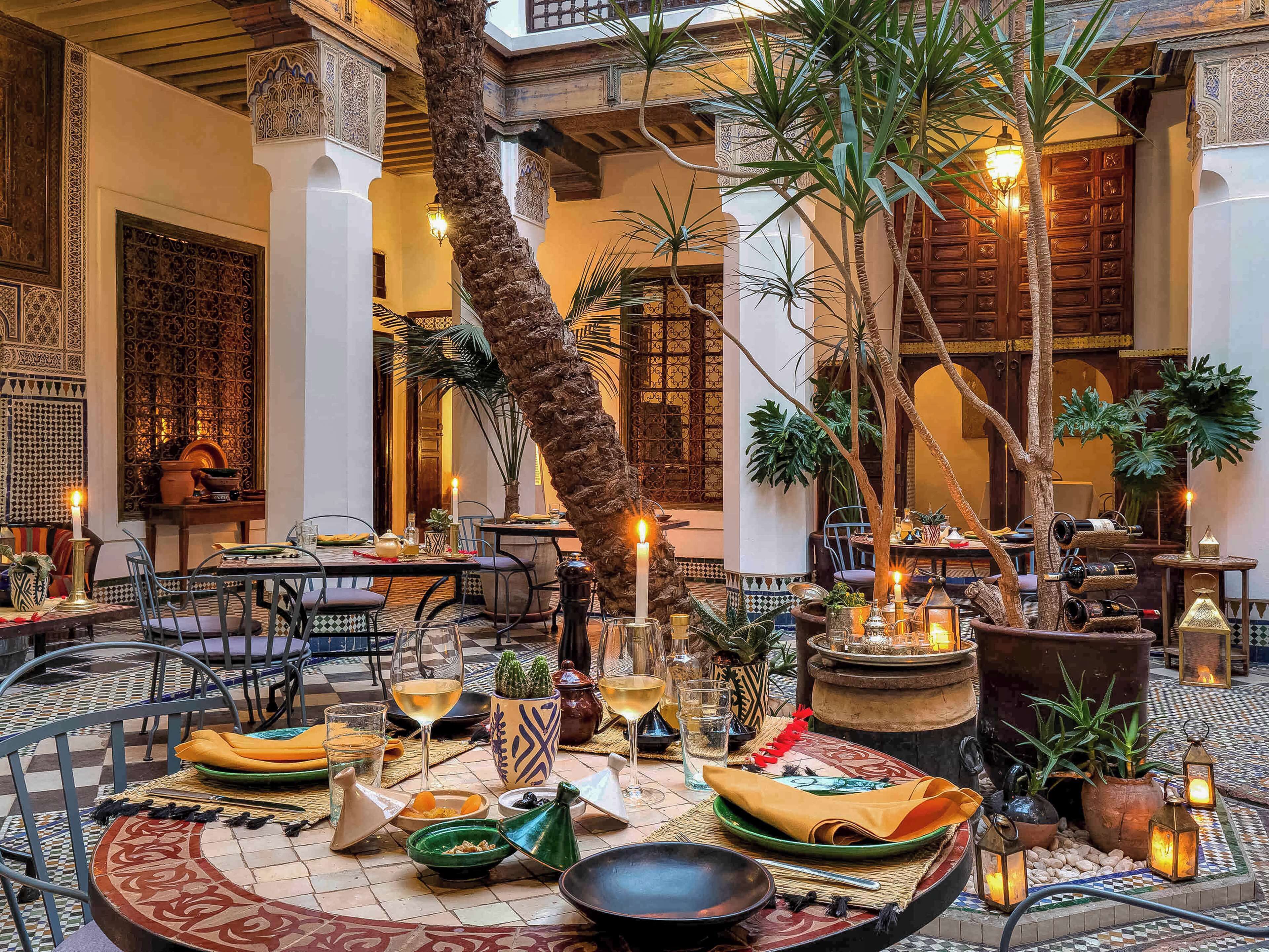 An indoor dining area with tables set for a meal, surrounded by decorative plants and traditional Moroccan decor.