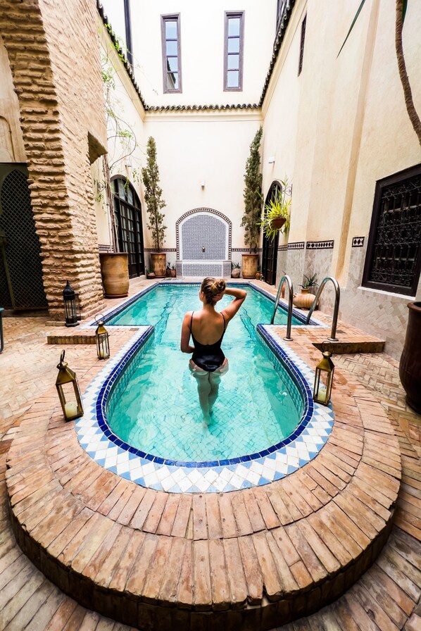 A pool with a tiled edge, surrounded by a brick deck, and a stone wall on one side.