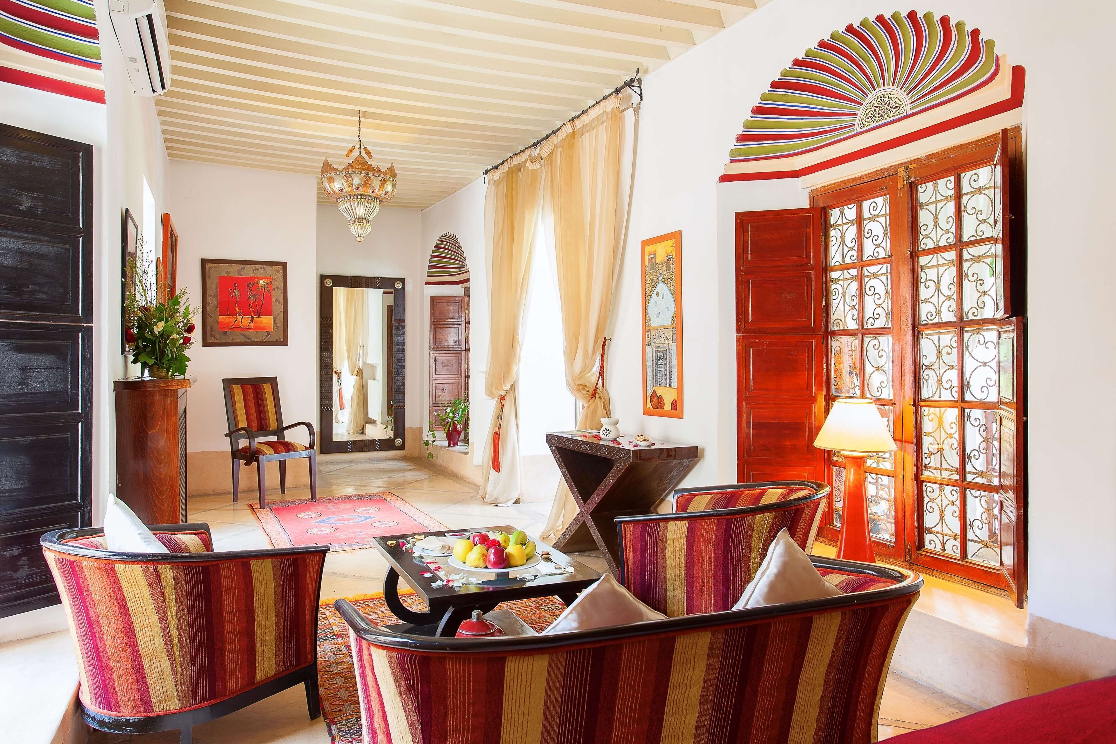 A room with a traditional design, featuring a large wooden door with glass panels, a chandelier, and a dining area with a table set for two.