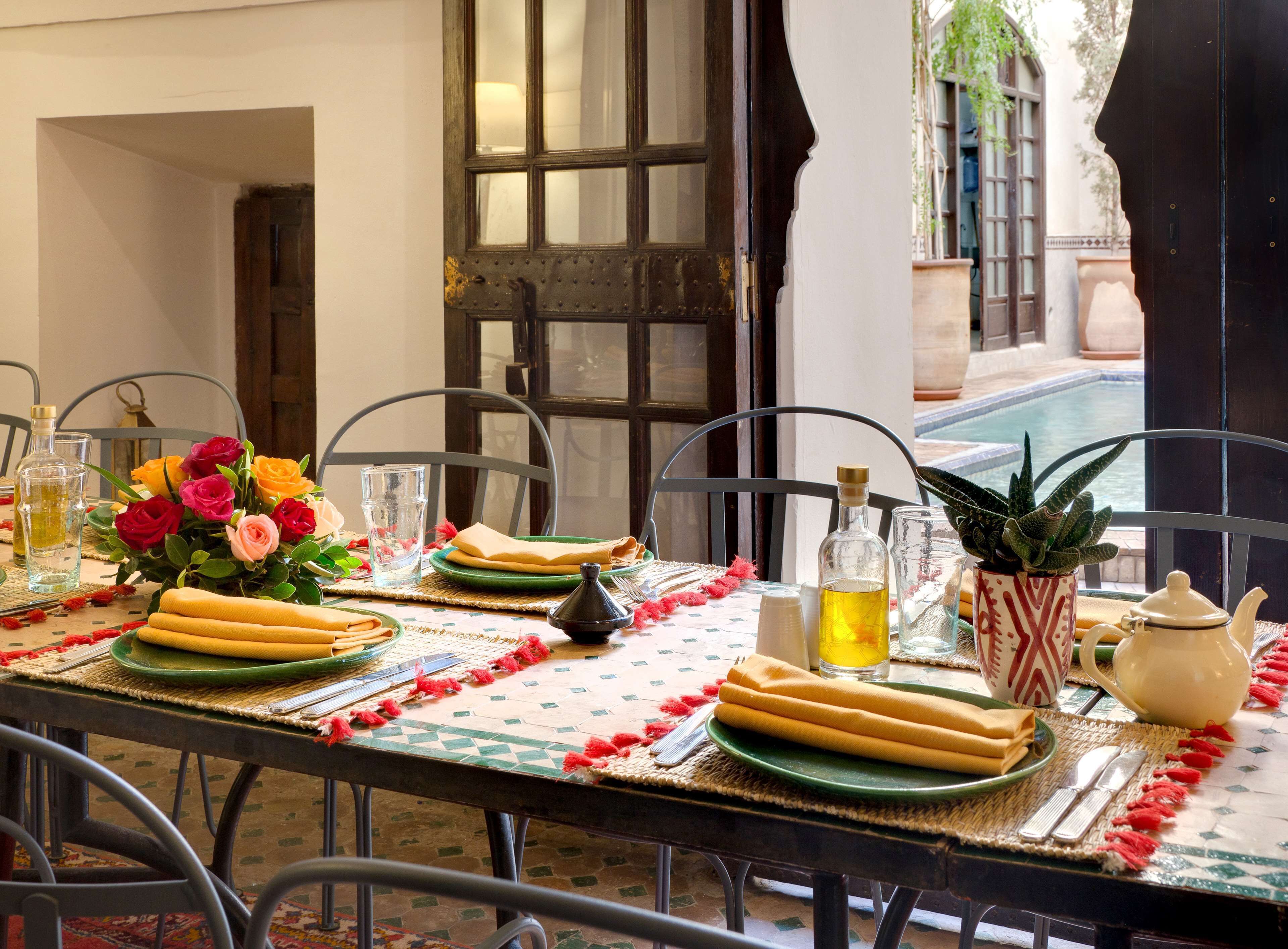 Une table à manger dressée avec des assiettes, des couverts, un vase de fleurs et une bouteille d’huile d’olive.