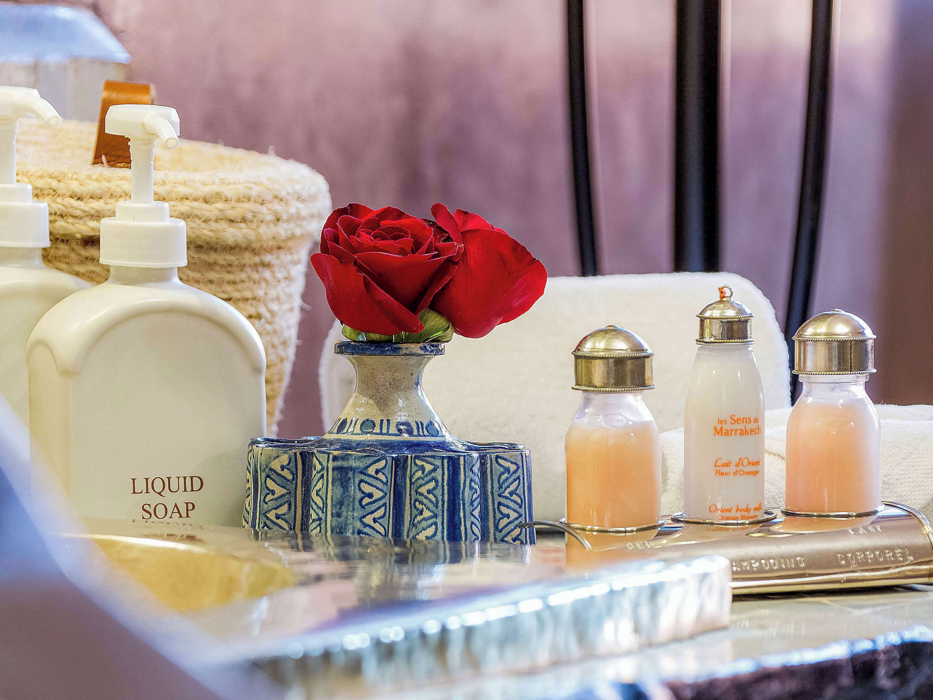 A bathroom with a bottle of liquid soap, a blue and white vase with a rose, and two salt and pepper shakers.