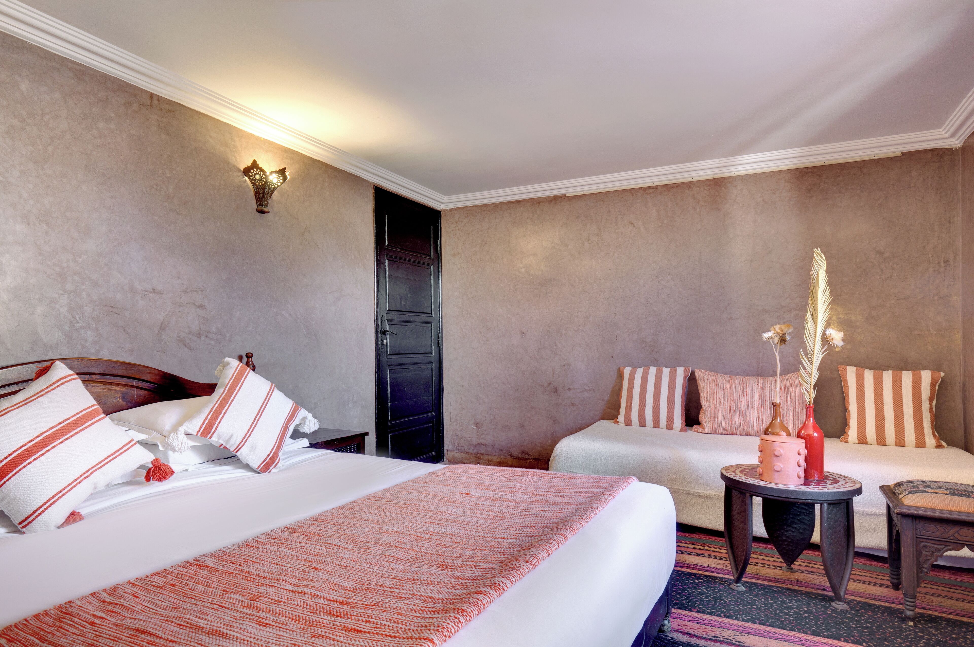A hotel room with a large bed, a smaller bed, a round side table, and a chair.