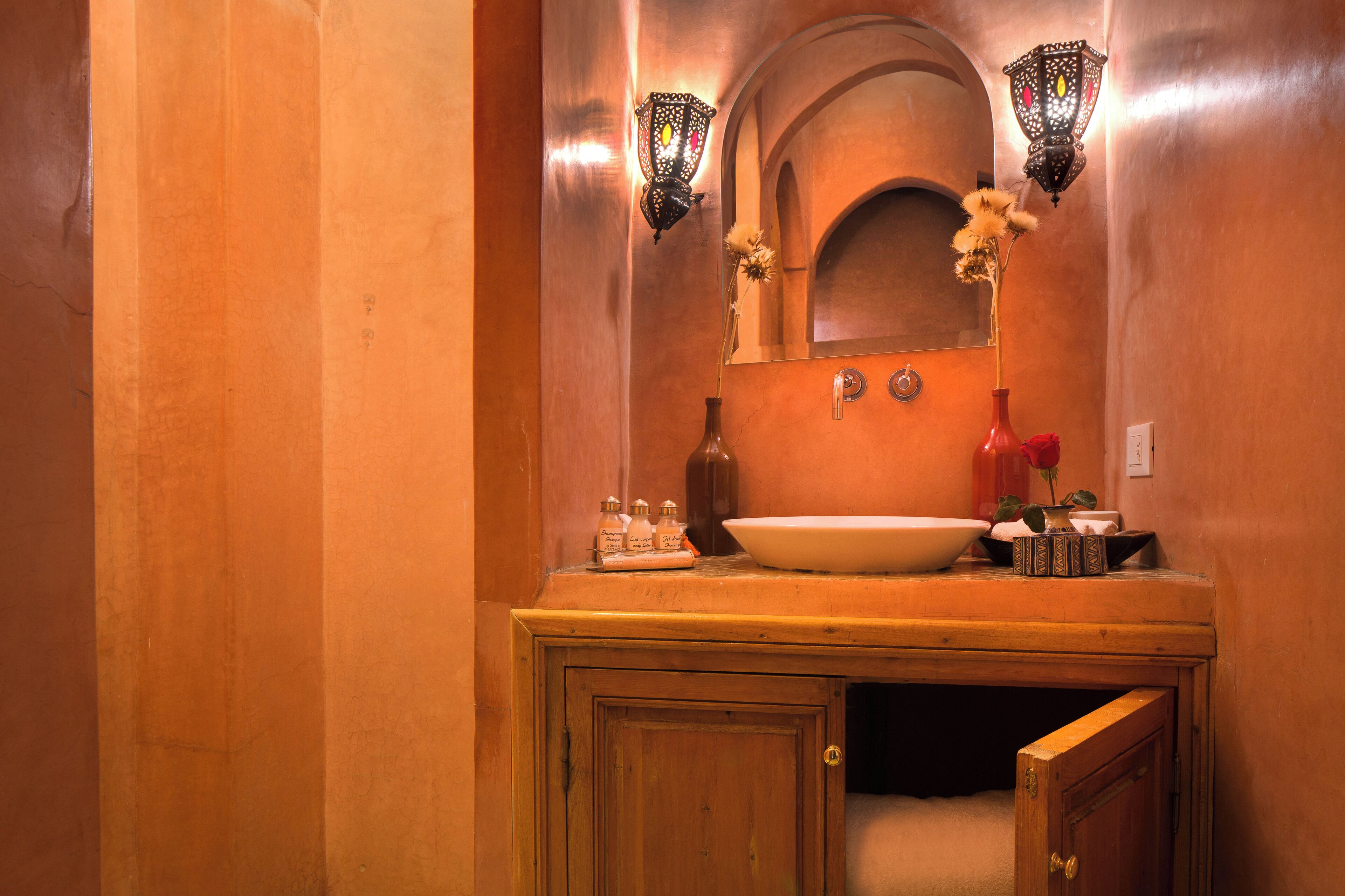 A bathroom with a wooden vanity, a large oval sink, two wall-mounted sconces, and a mirror above the vanity.