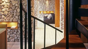 A spiral staircase with a wooden finish, leading to a stone-walled room with a built-in fireplace and a cozy seating area.