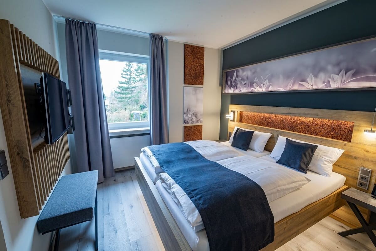 Una habitación de hotel moderna con una cama grande, un escritorio, un televisor y un ventanal con cortinas.