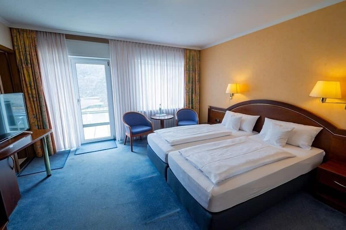 Habitación de hotel con una cama grande, dos mesitas de noche, un escritorio con una silla, una pequeña mesa con dos sillas y un televisor.