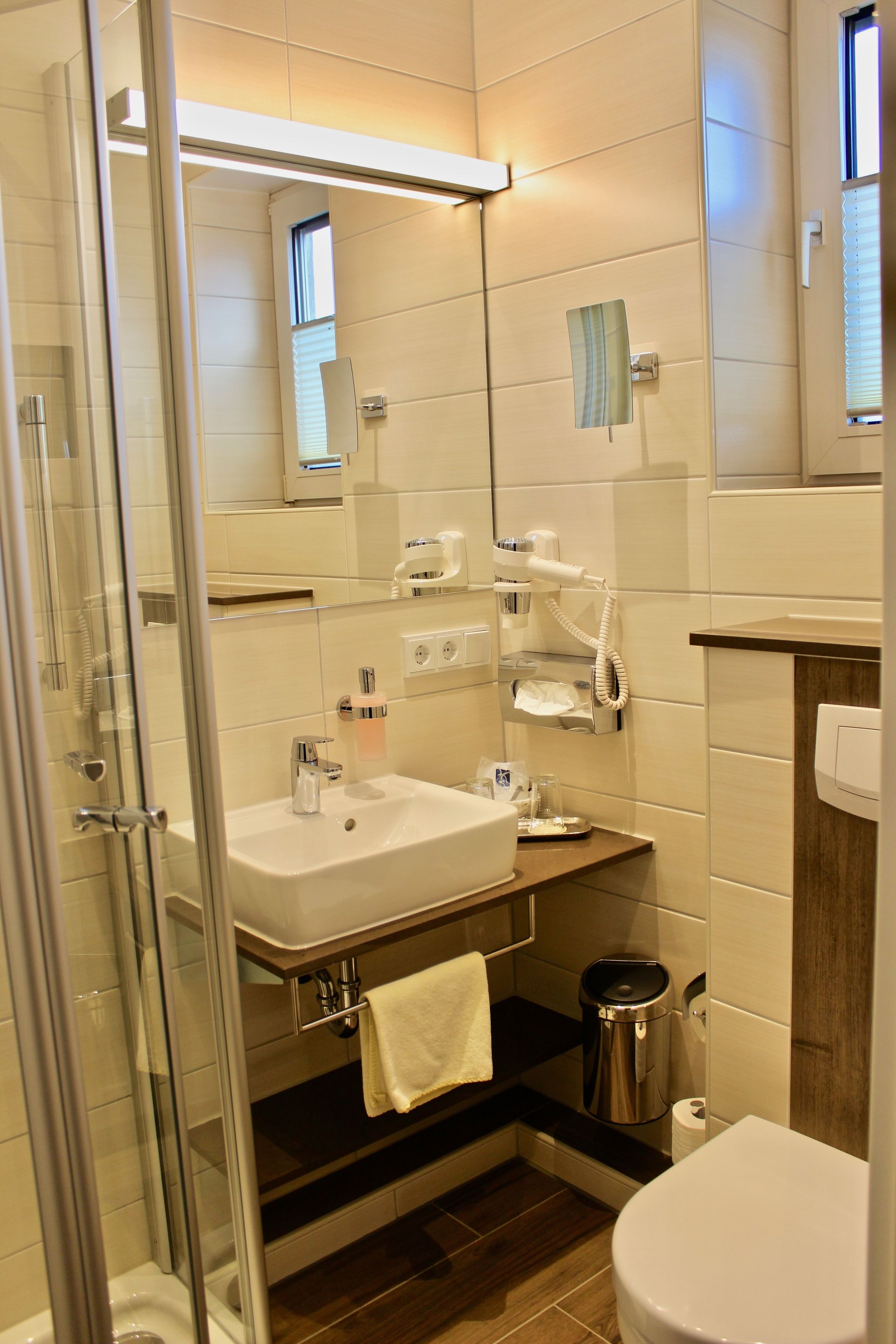 A modern bathroom with a glass shower enclosure, a sink with a vanity, a toilet, and a trash can.