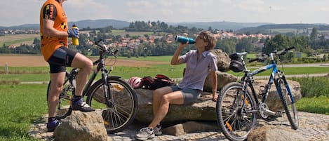 Two people sitting on rocks with bicycles, overlooking a rural landscape.