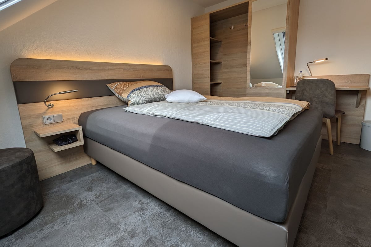 A modern bedroom with a large bed, a bedside table, a desk, and a wardrobe.