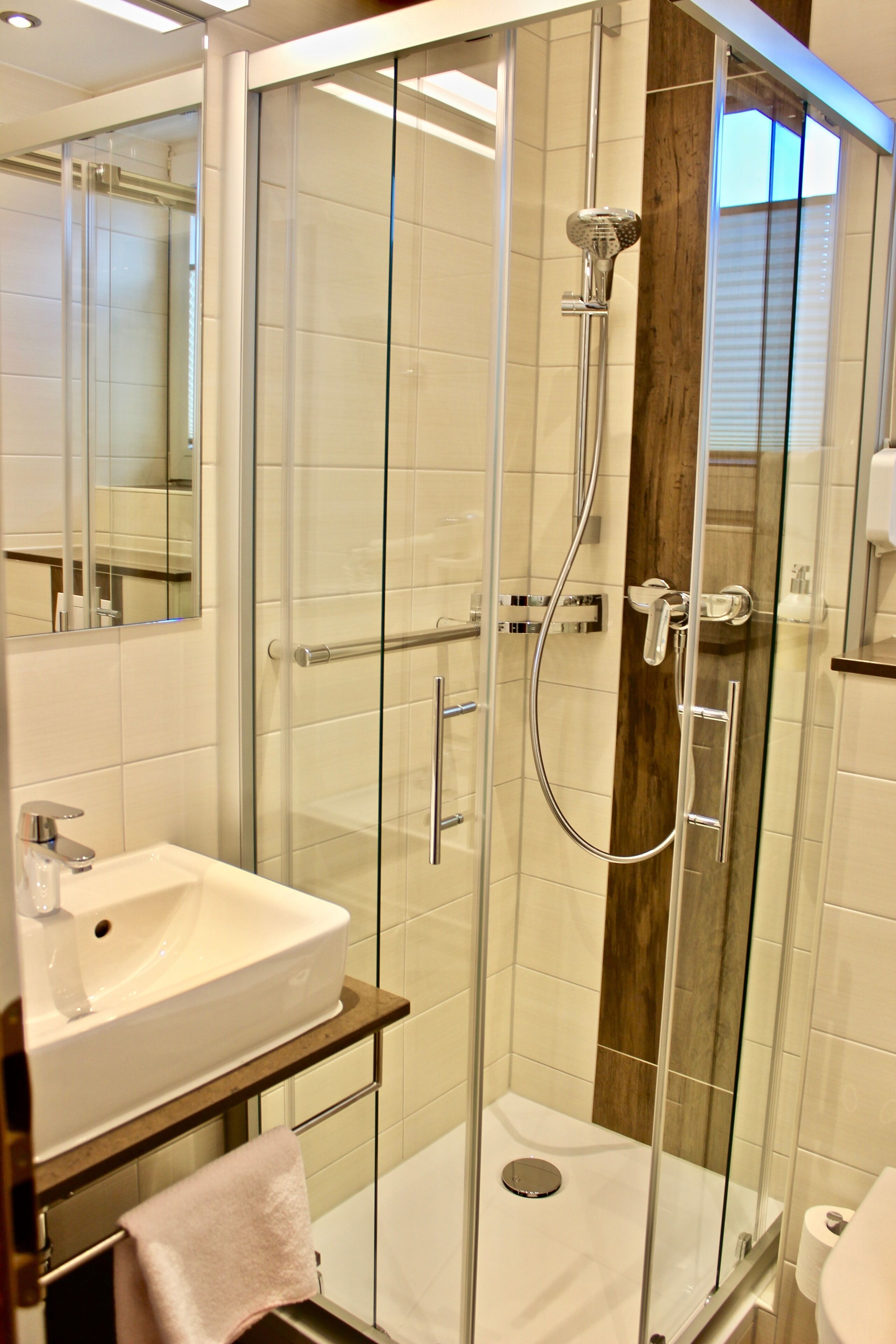 A modern bathroom with a glass-enclosed shower, a white sink, and a wooden vanity.