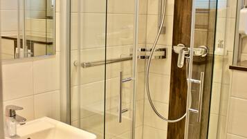 Een moderne badkamer met een douchecabine van glas, een witte wastafel en een houten opbergmeubel.