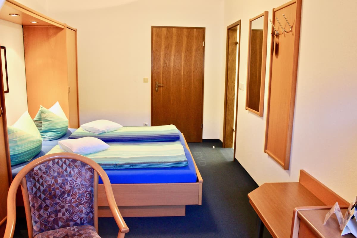 A hotel room with a bed, a chair, a desk, and a door.