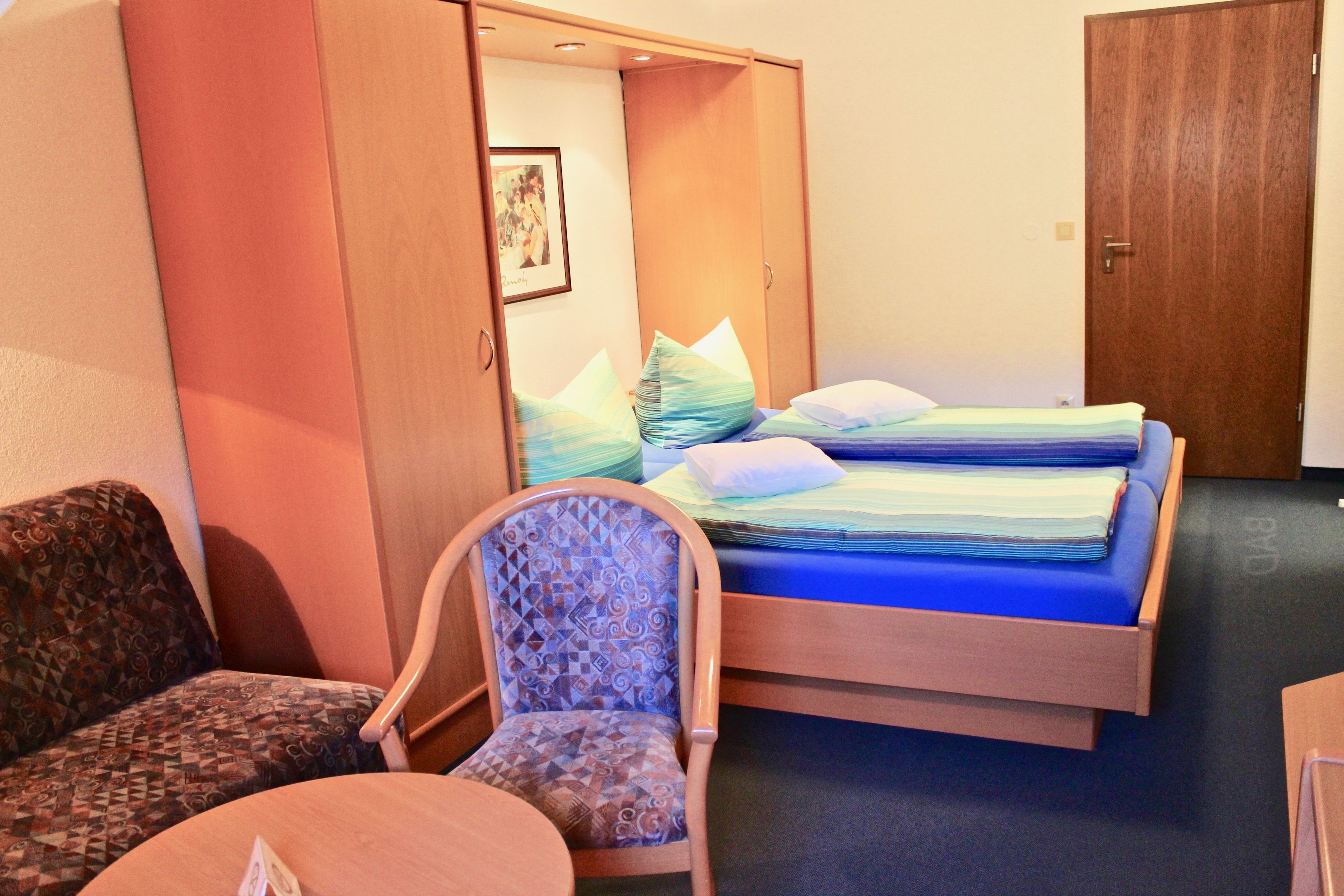 A hotel room with a bed, a chair, a table, and a wardrobe.