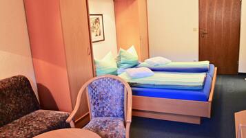 A hotel room with a bed, a chair, a table, and a wardrobe.