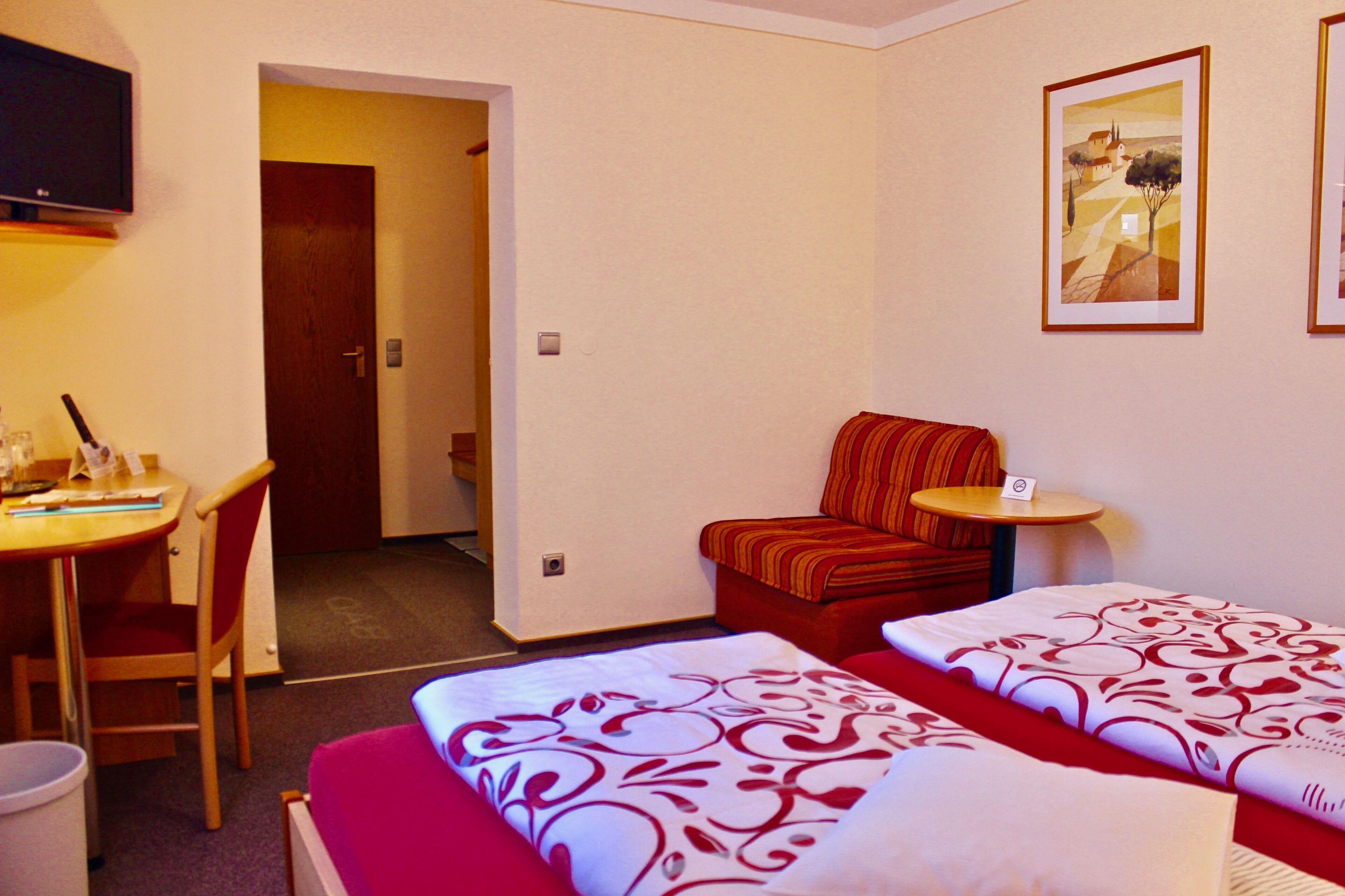 Ett hotellrum med två sängar, ett skrivbord, en stol, ett litet bord och en TV.