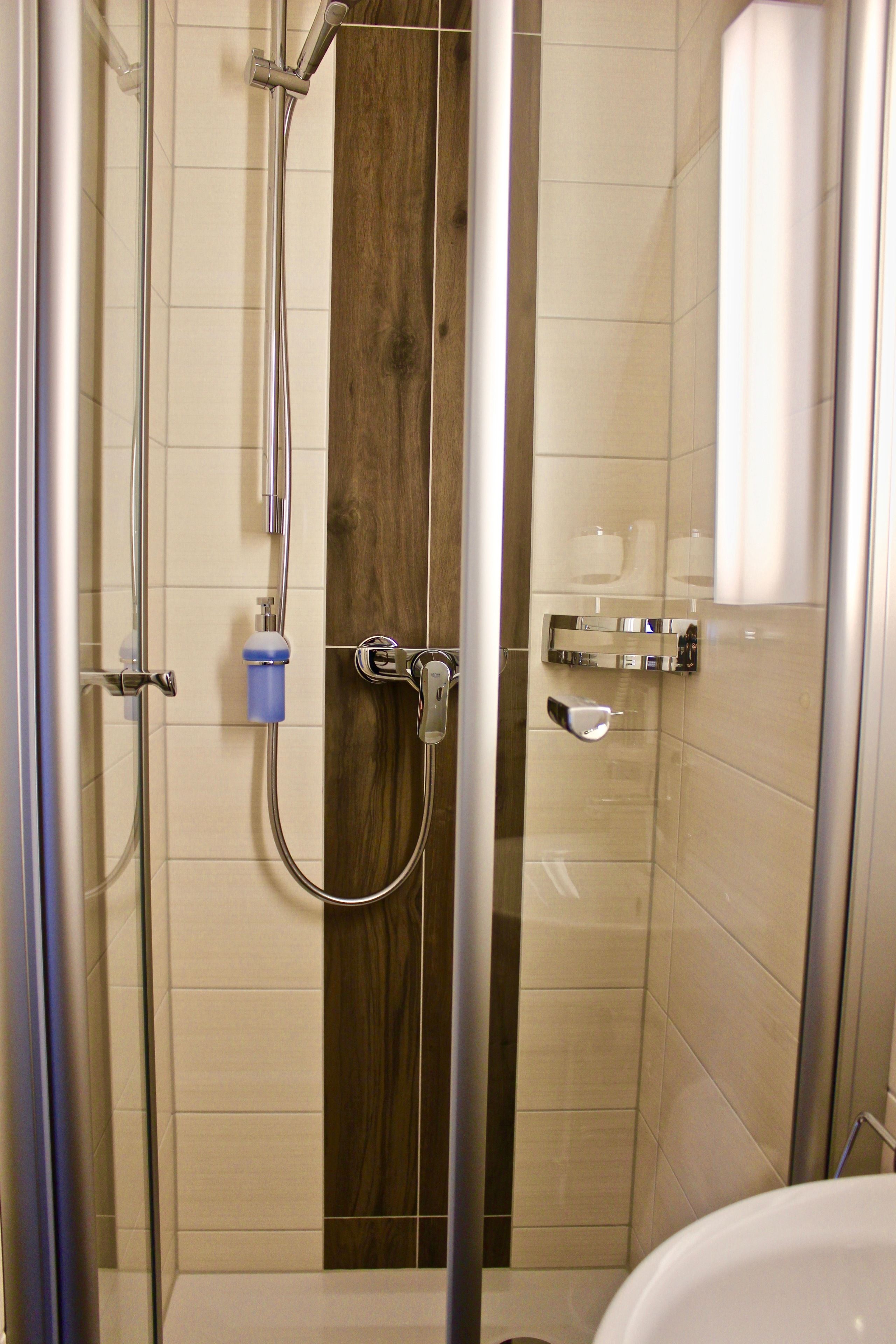 A shower with a wooden panel, a glass door, and a white bathtub.