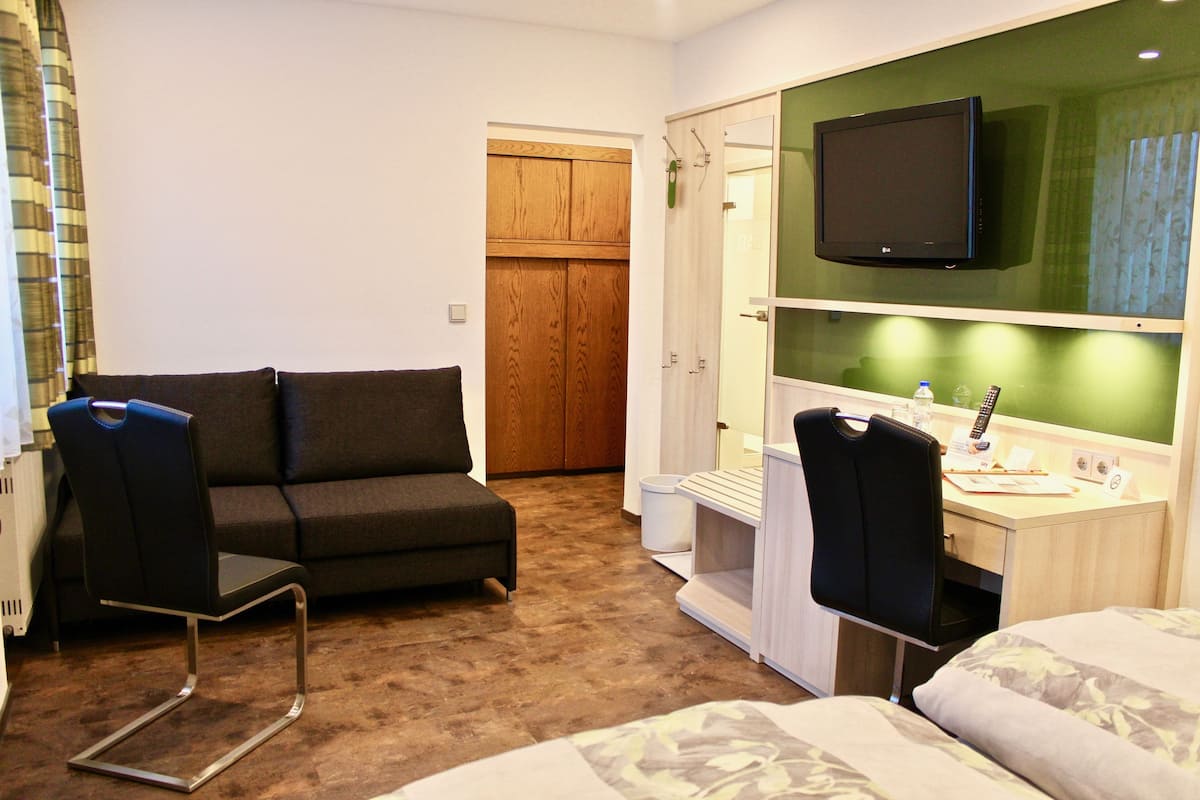 A hotel room with a sofa, a desk with a chair, a bed, a television, and a wardrobe.