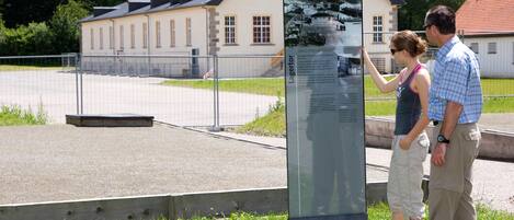 A historical building with a traditional architectural style, a paved area in front, and a metal information kiosk.