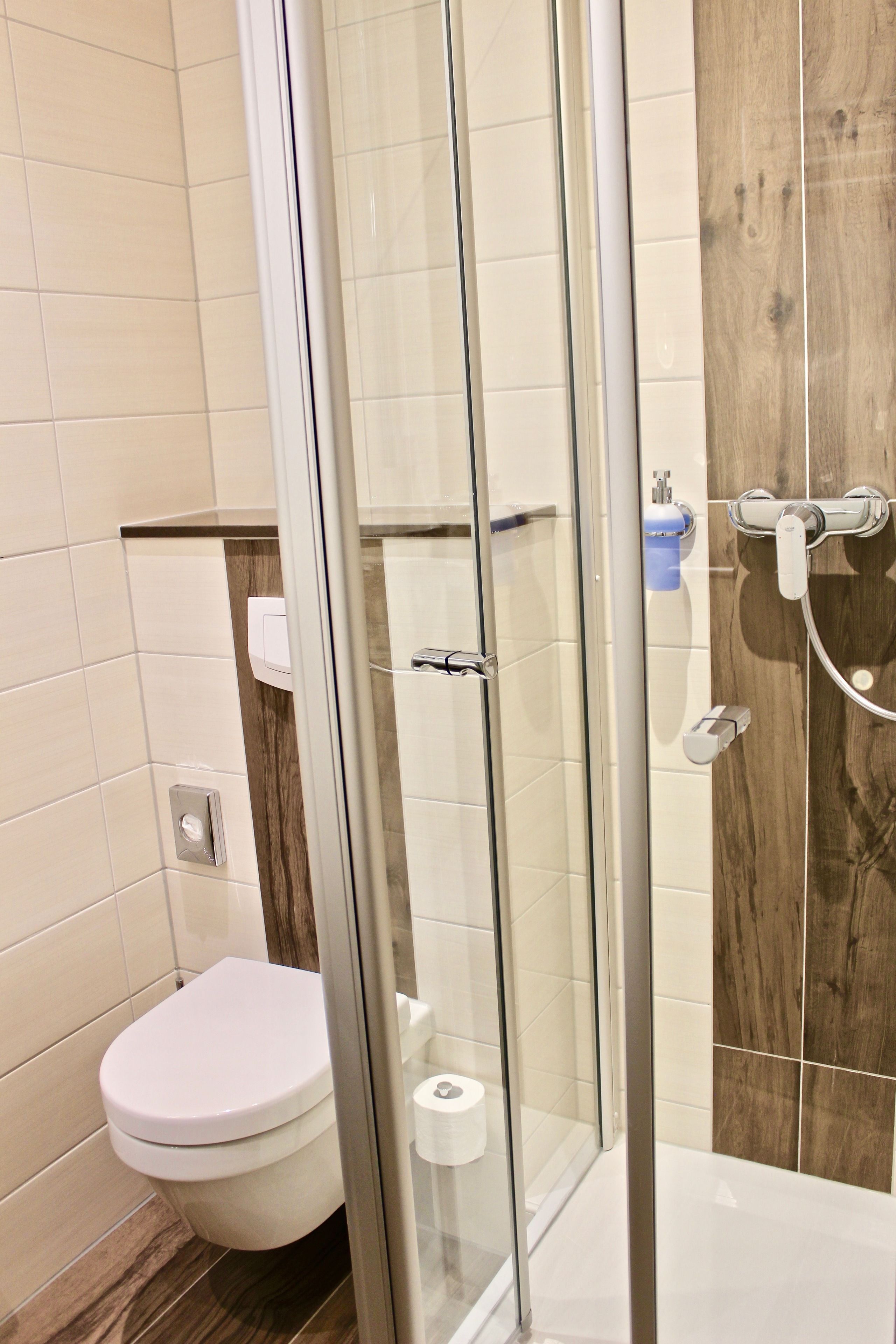 Een moderne badkamer met een douchecabine van glas, een toilet en een wand met houten accenten.