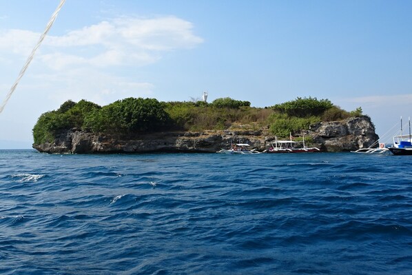 A rocky island with boats docked at its base, surrounded by clear blue water.