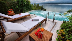 Un espace piscine paisible, doté de chaises longues et d’un jacuzzi, offrant une vue sur un lac tranquille et des montagnes lointaines.
