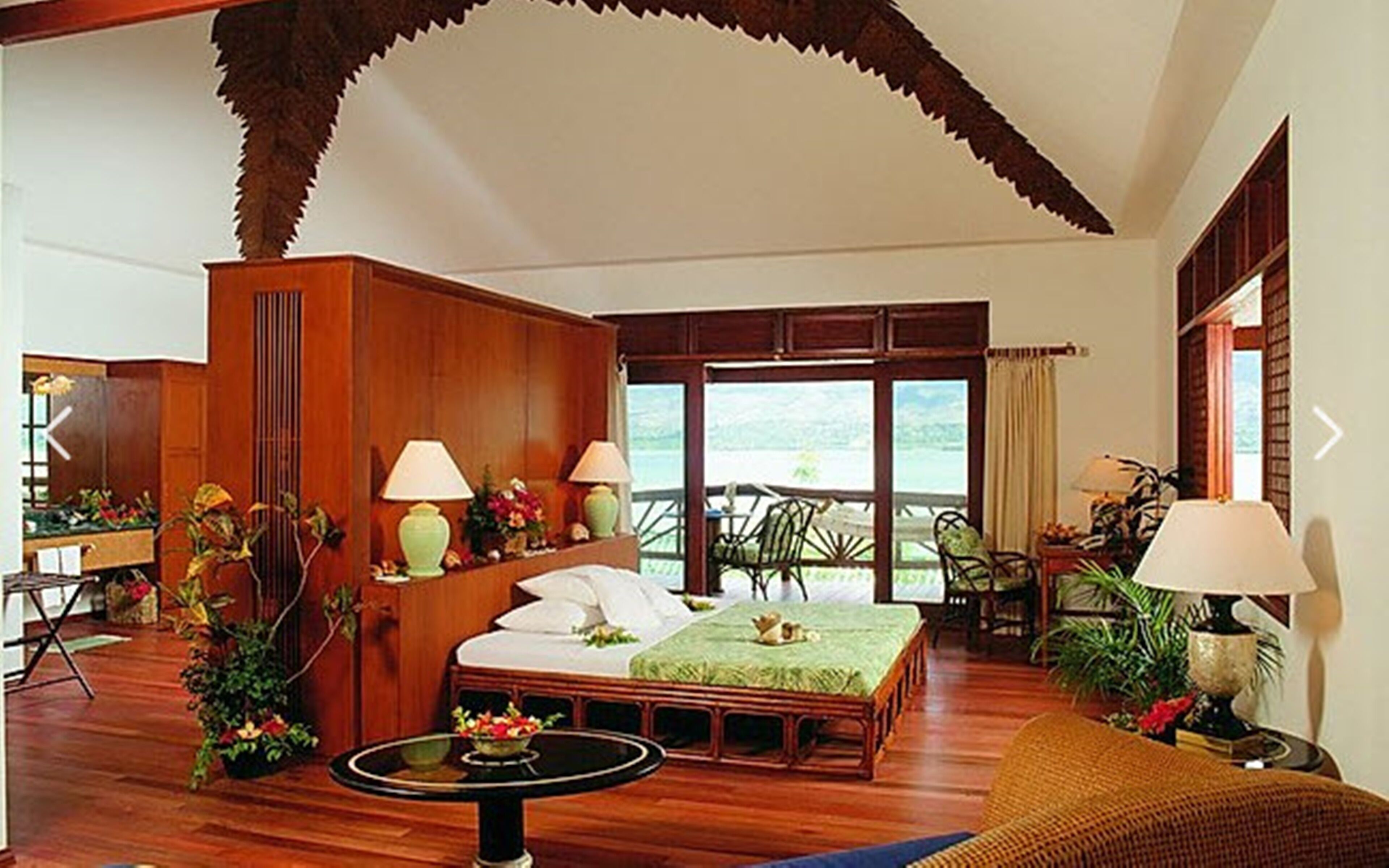 A spacious bedroom with a large bed, a sitting area with a table, and a balcony with chairs.