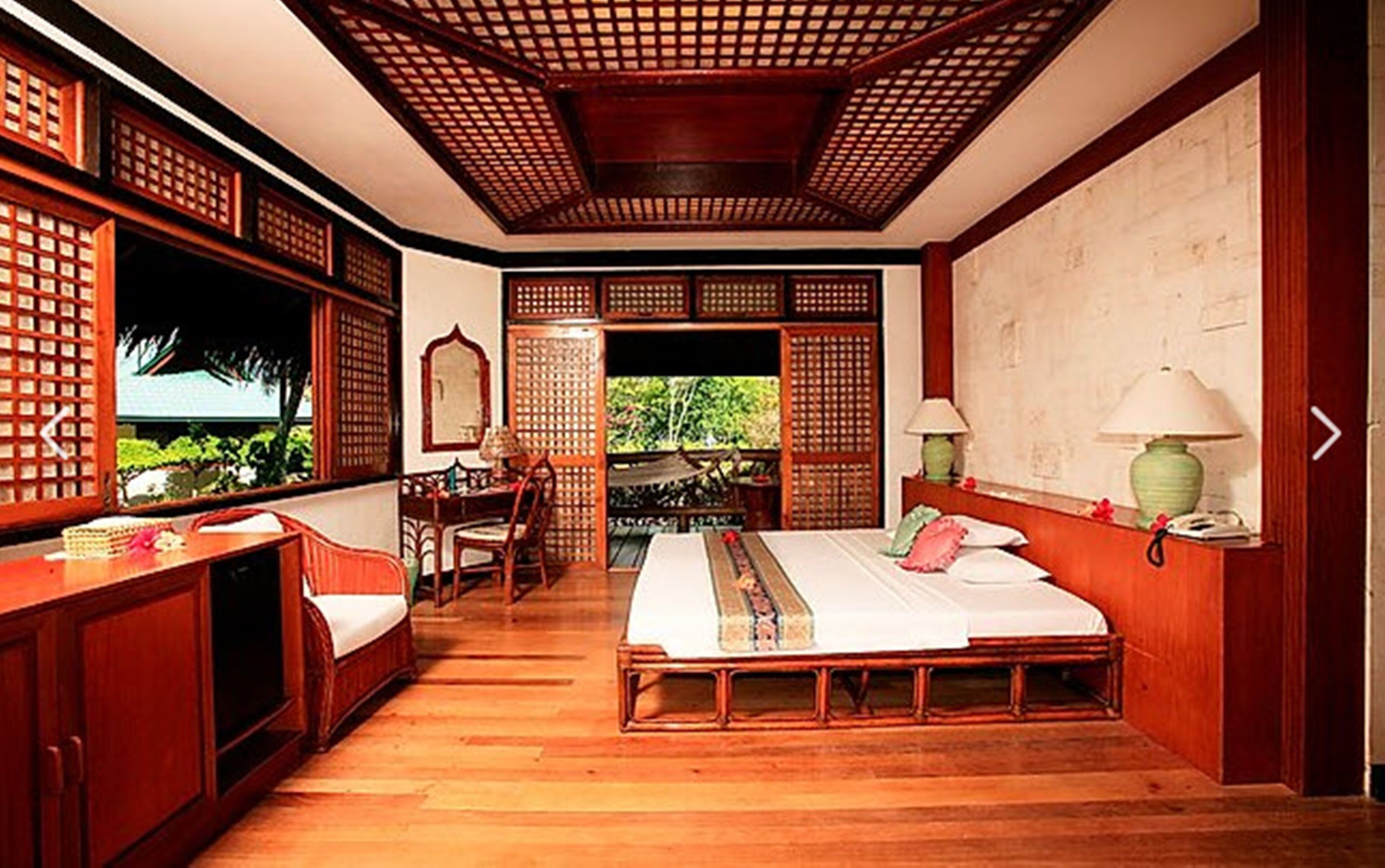 A traditional room with a bed, desk, chair, and a view through a lattice door.