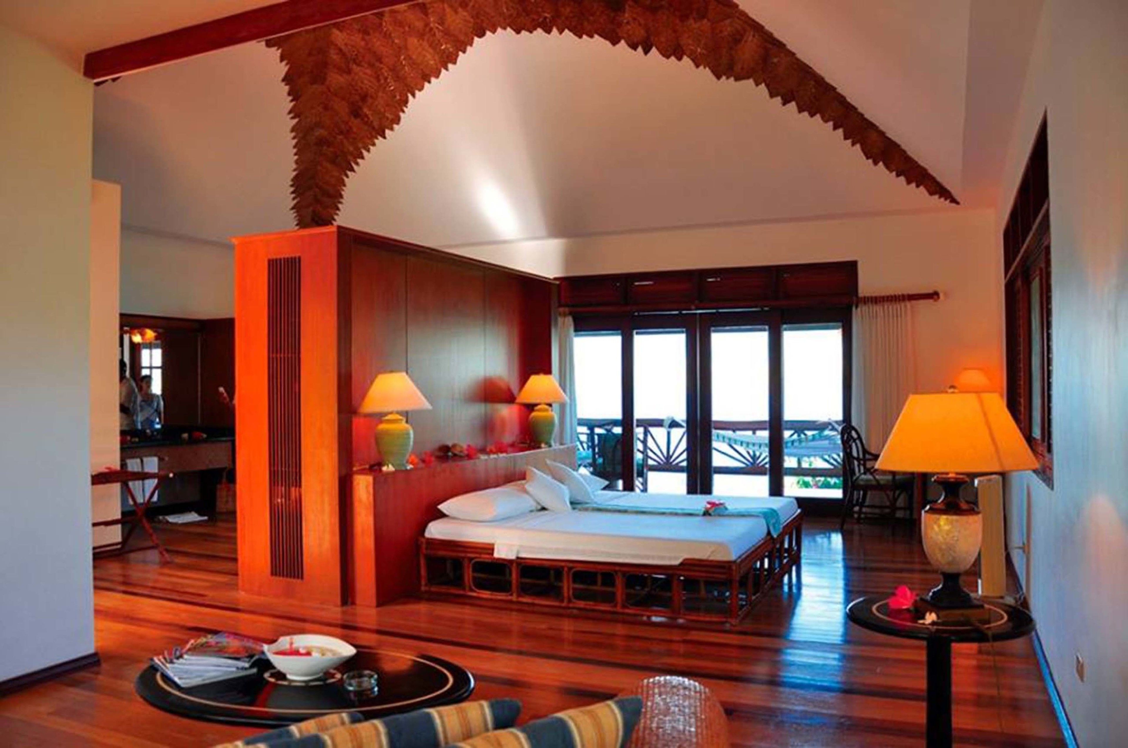 Une pièce spacieuse avec un grand lit, deux lampes de chevet, un plafond en bois et un balcon avec vue.