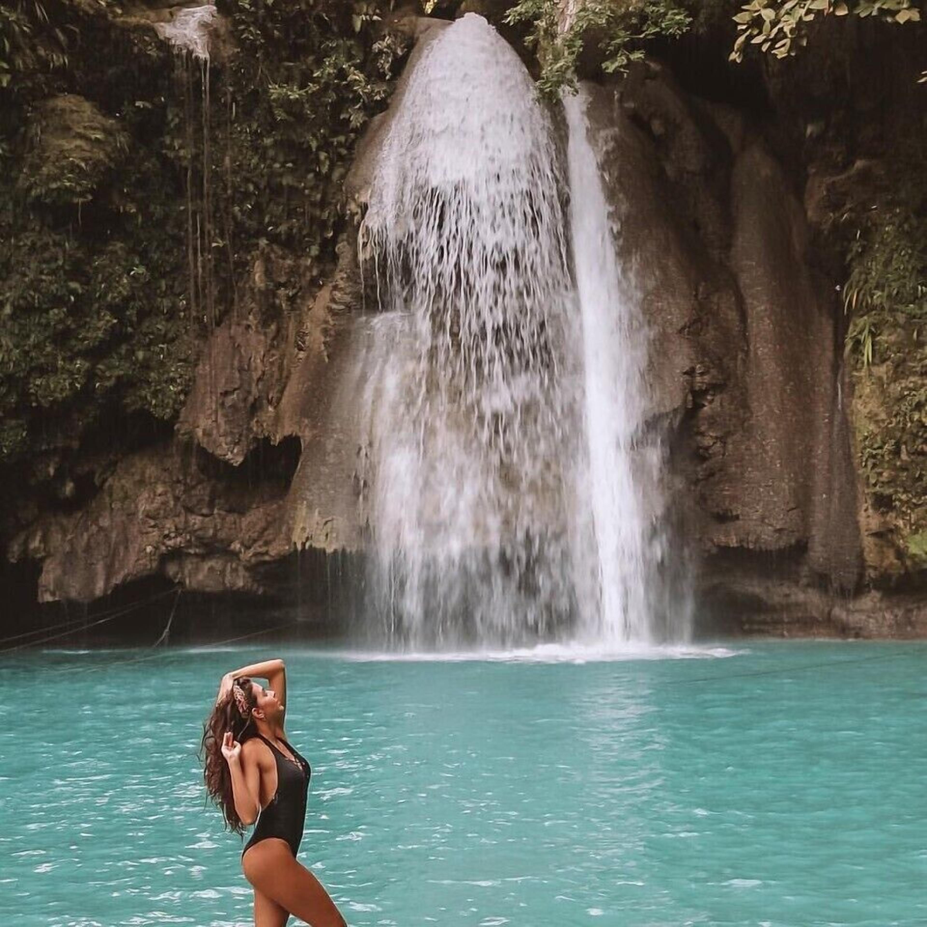 A woman in a swimsuit standing in a pool with a waterfall in the background.